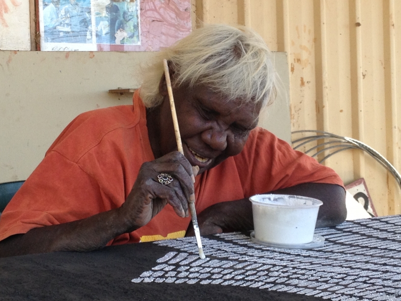 Warmun artist Lena Nyadbi smiling while painting white dots on a canvas.