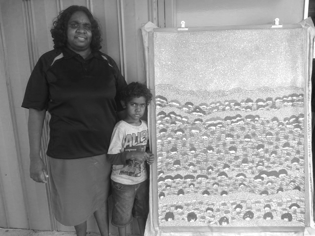 Black and white artist Yvonne Bonney from Artists of Ampilawatja standing with a young child next to her painting.