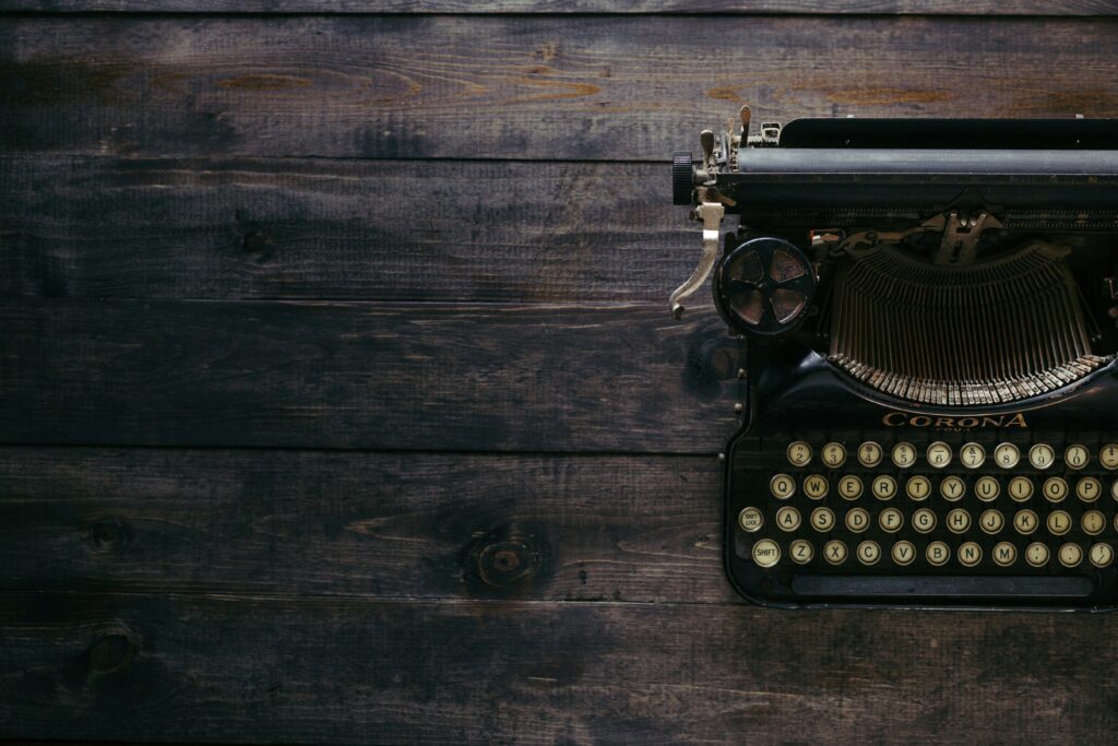 A birds-eye photograph of a black typewriter atop of a dark, wooden bench.