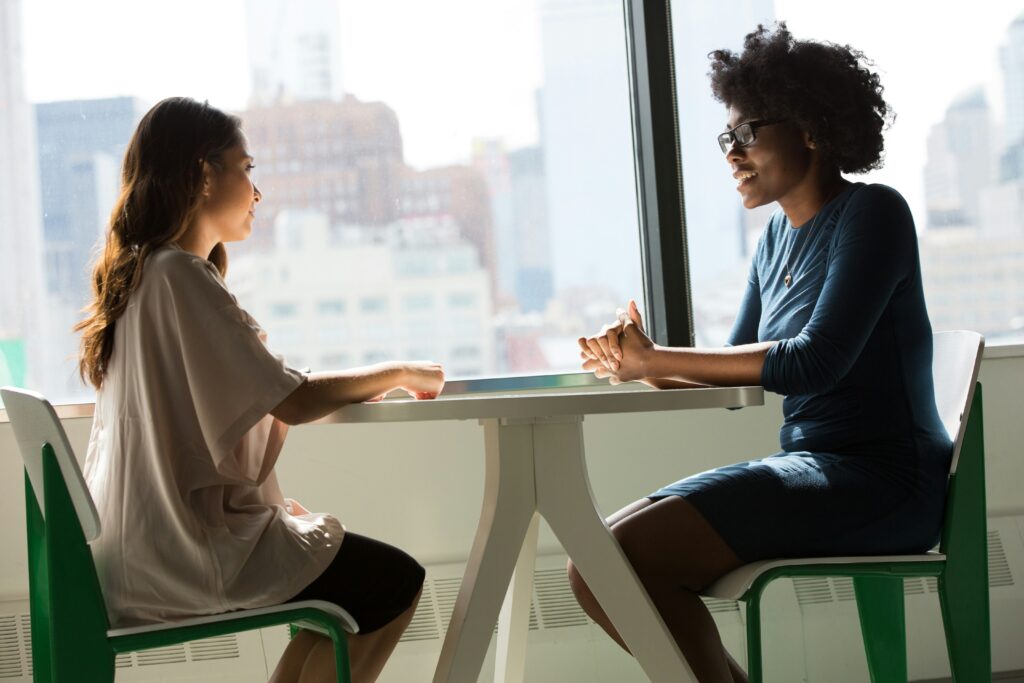 Two women speaking across a table in a corporate office.