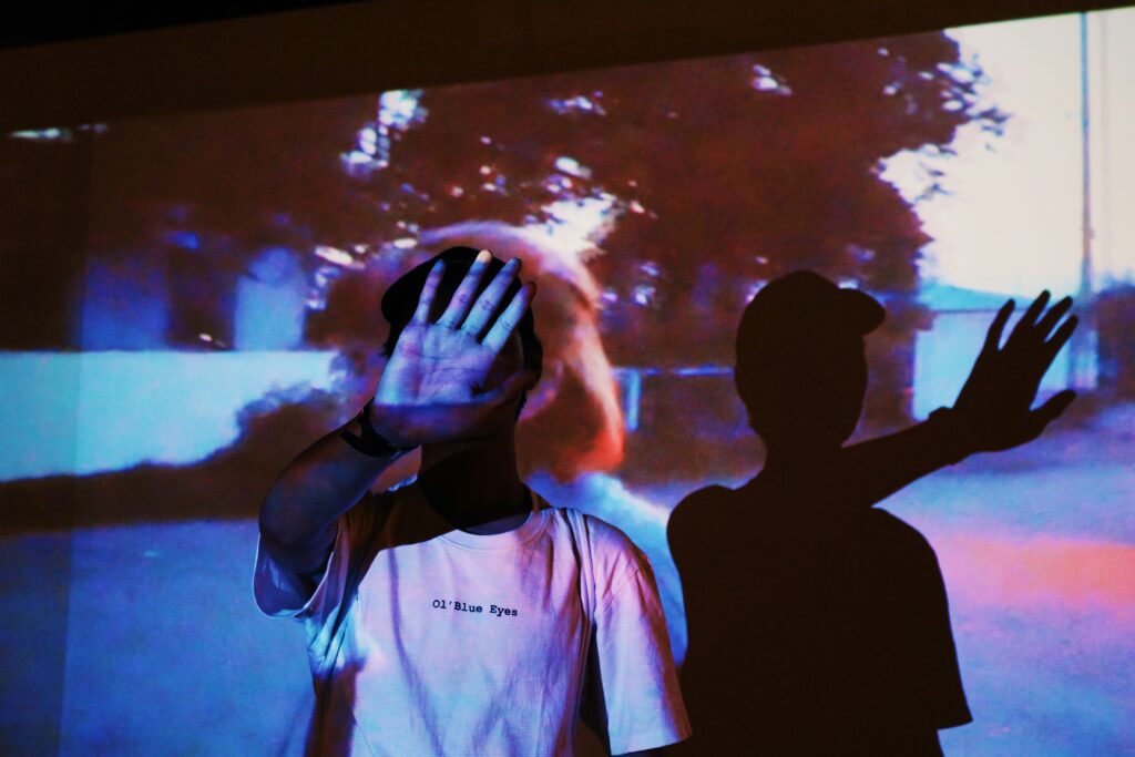 A photograph of a man and backdrop illuminated by a projected image