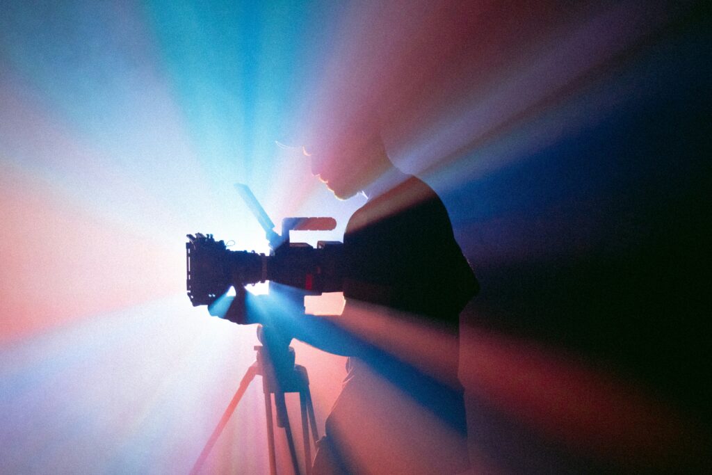 A photograph of a silhouetted cameraman, with pink and blue light beams surrounding him