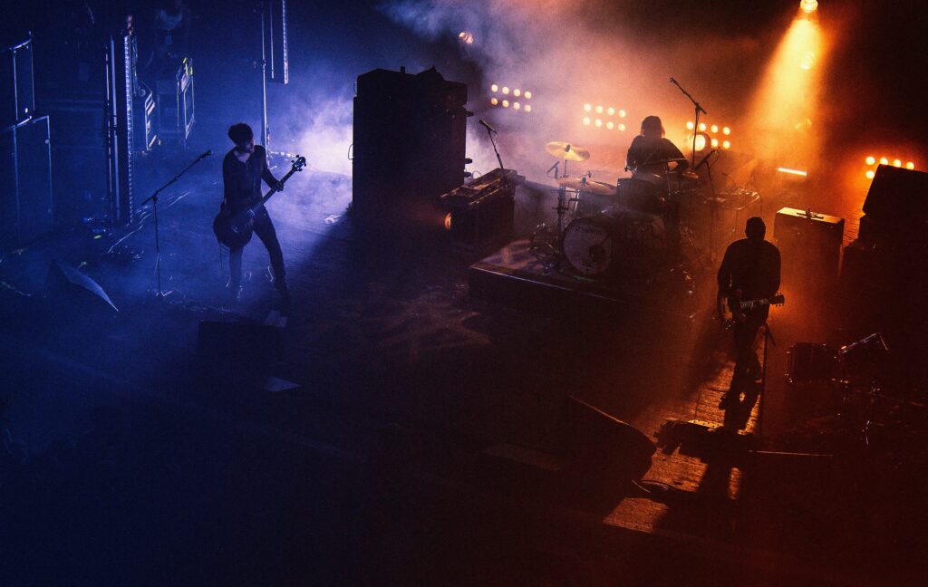 A photography of a band on a dark, smoky stage with purple and orange lighting backlighting them