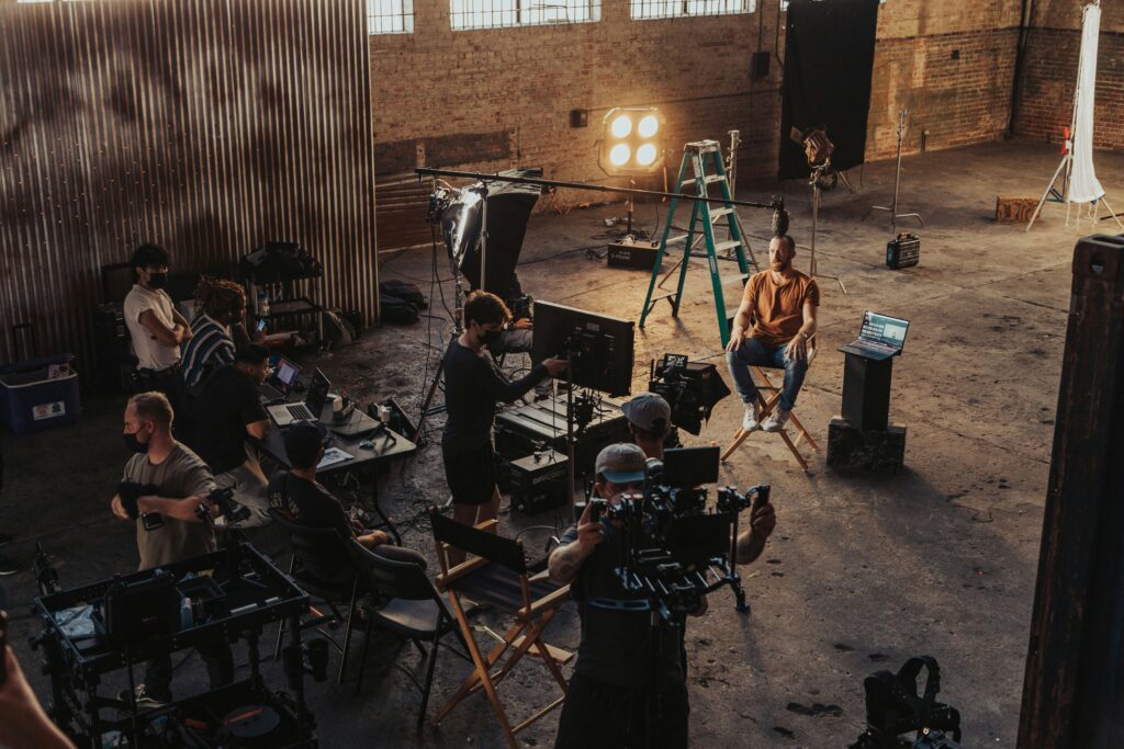 A wide photograph of a busy film set and a man prepared to be interviewed