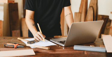 Photo of cropped man working on laptop in woodwork workshop