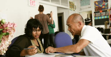 Photo of Asian man helping a woman fill out paperwork.