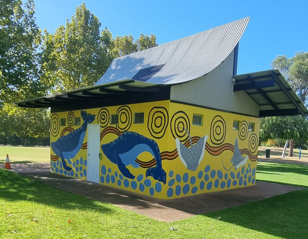 A mural painted on a small council building. The mural has whales and dolphins on a yellow background.