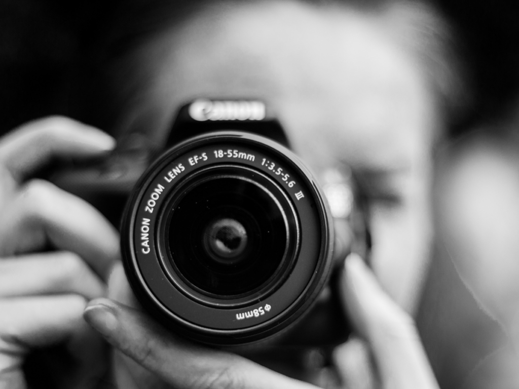 A black and white photograph of a woman holding a DSLR camera.